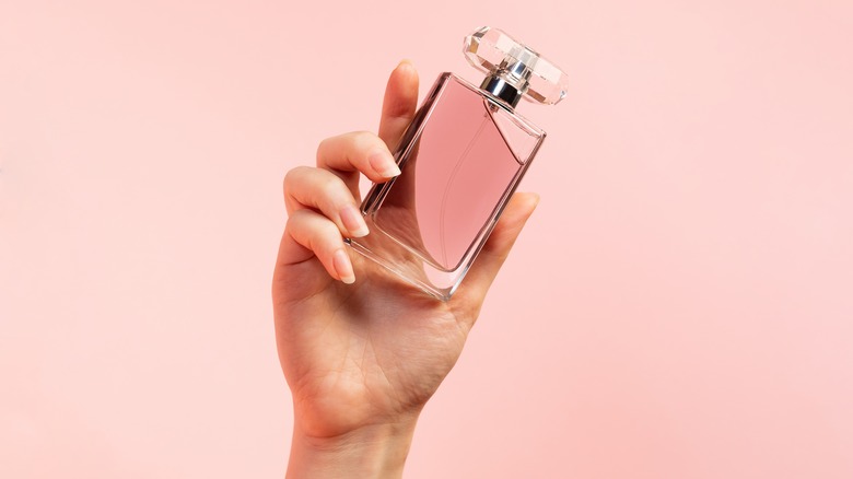 Woman holding perfume, pink background