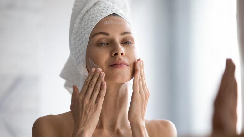 close up of woman in bath towel applying skincare
