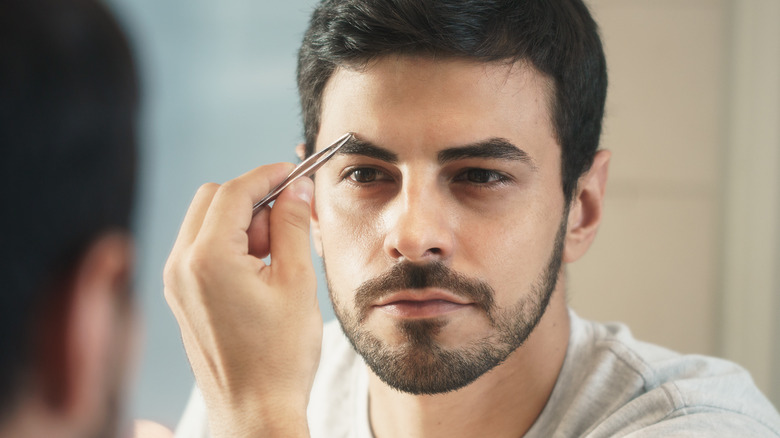 Man plucking eyebrows in mirror