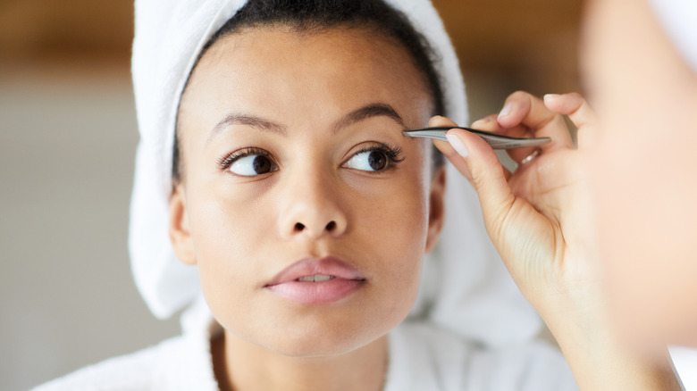 Woman plucking eyebrows with hair in towel