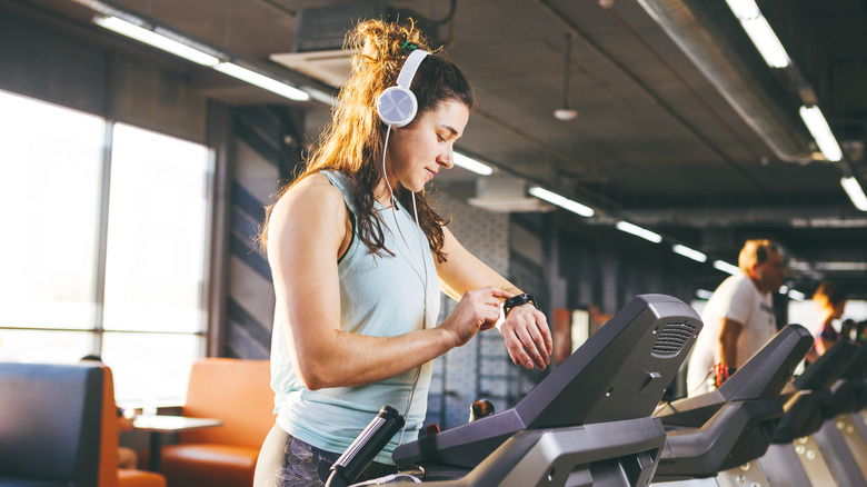 Woman wearing headphones, checking fitness watch, while on treadmill