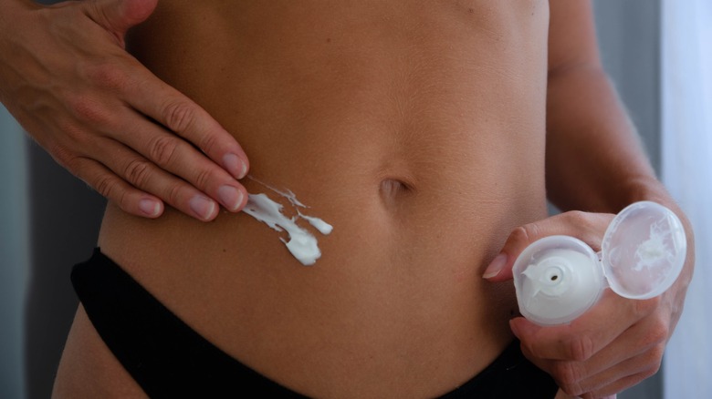 woman rubbing lotion on stomach 