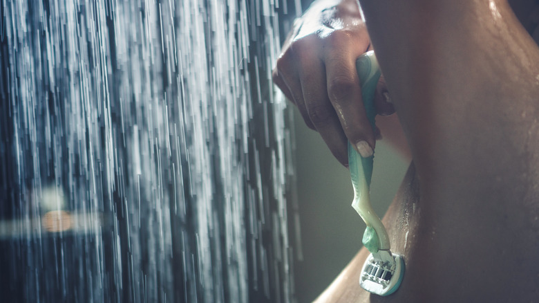 Person shaving underarms in shower