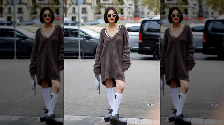 A person posing in a brown sweater dress with knee-high socks.