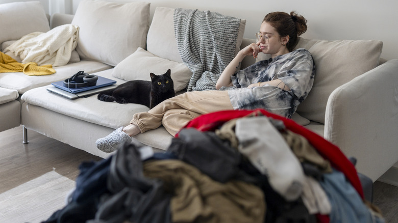 A woman sitting on a sofa, ignoring a pile of laundry.