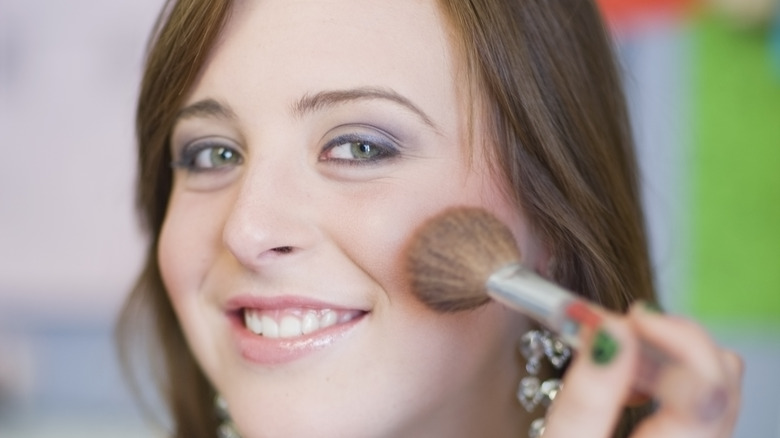 woman applies blush to cheek