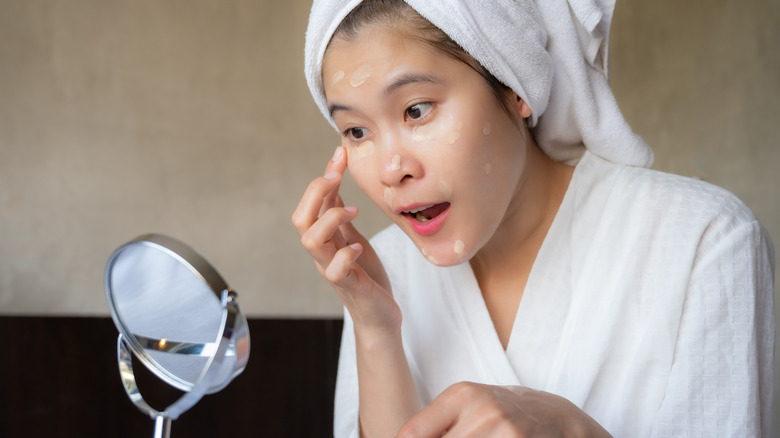 woman applying concealer in mirror