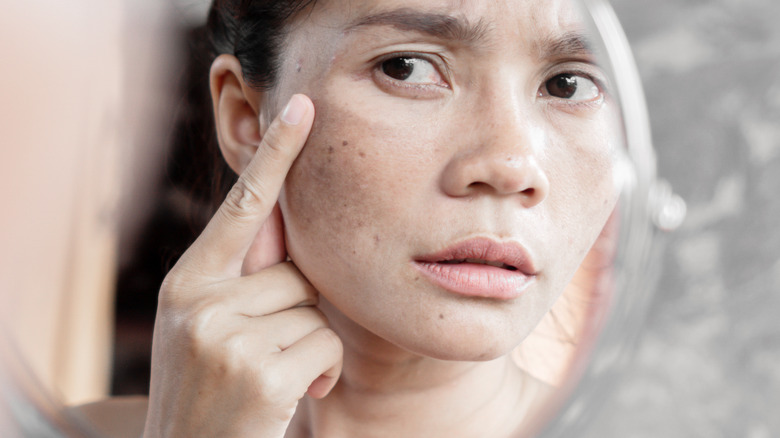 woman examining face in mirror