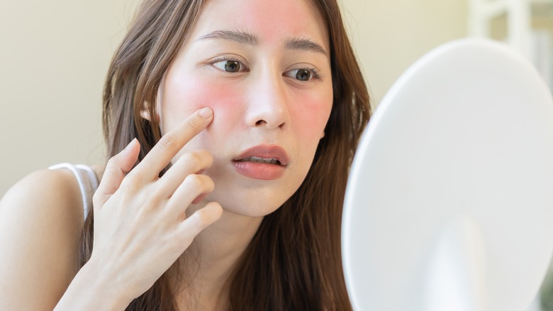 flushed woman looking at her face in mirror