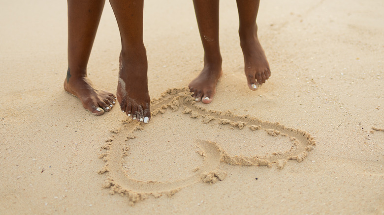 Two people drawing heart in sand with toes