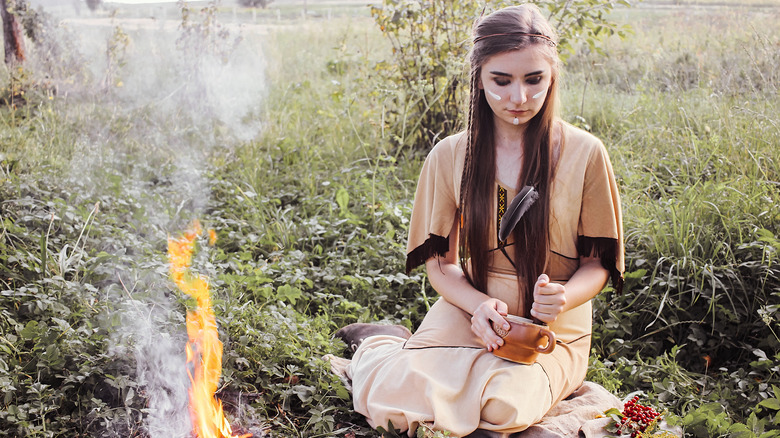 Woman grinds sacred herbs next to fire