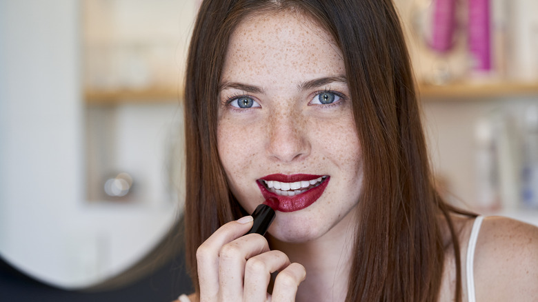 Woman applying dark red lipstick