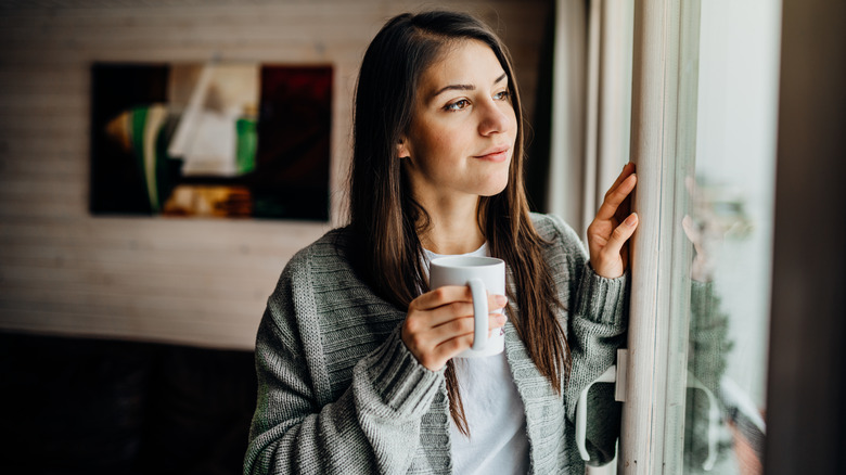 woman holding coffee looking out window