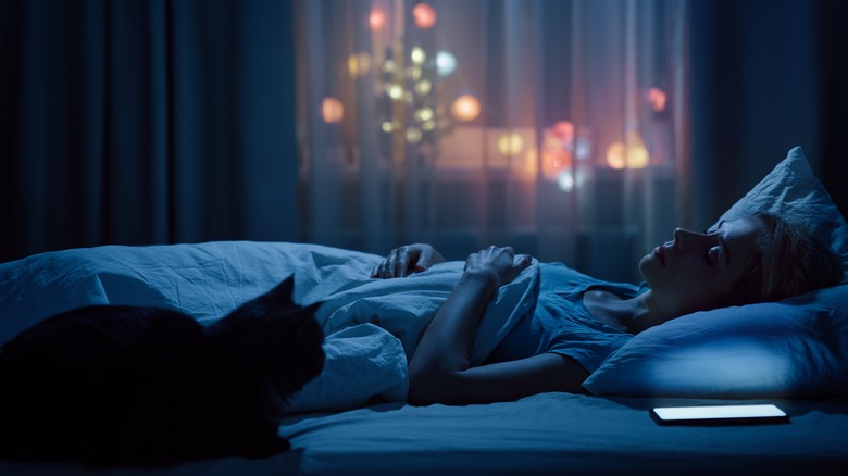 Woman sleeping next to phone and cat in bed
