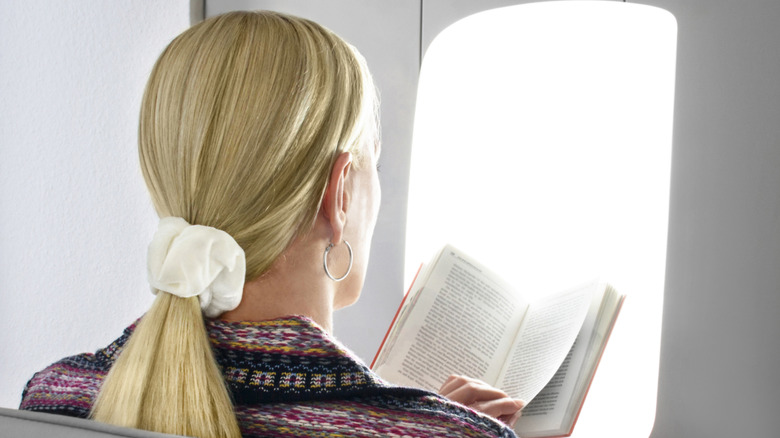 Woman reading book in front of light therapy lamp