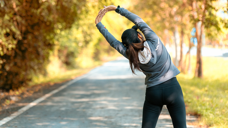 Woman stretching while walking alongside path