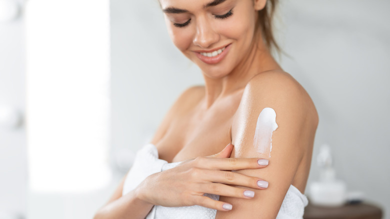 Woman in towel applying skin cream to arms
