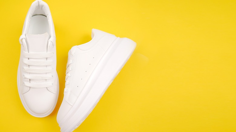 white leather shoes laying down against yellow background